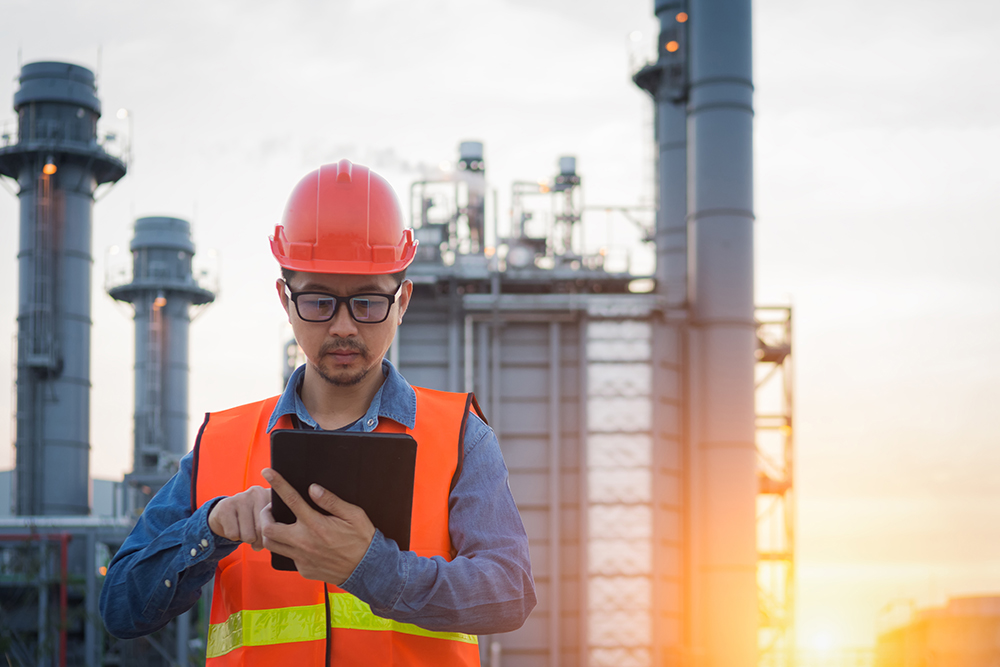 Oil and gas worker checking information on wireless tablet enabled by ERRCS Public Safety Communication systems installed through RFE Communications